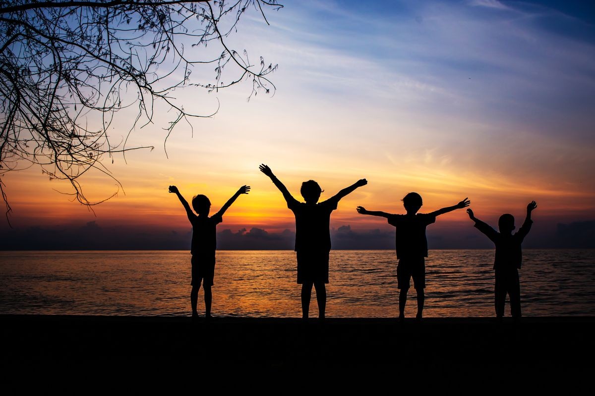 Silhouette of the four  kids are raise hands up against sunrise at the beach, praise and worship or travel concept